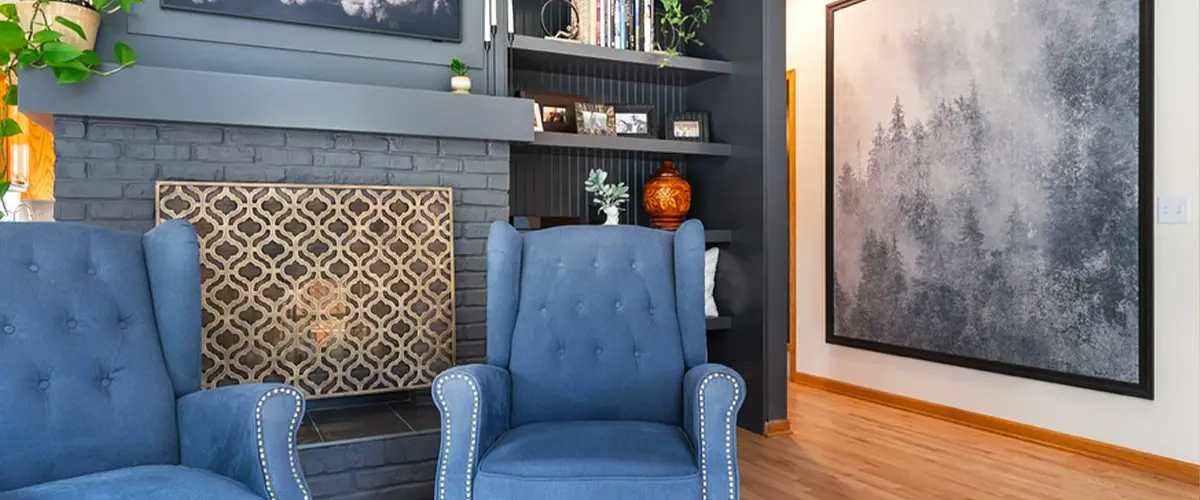 Cozy living room with blue armchairs, a dark gray fireplace, floral artwork, and built-in bookshelves.