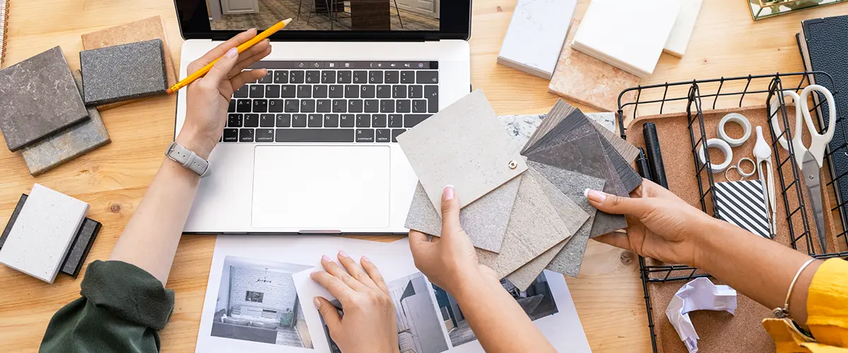 Hands selecting tile samples and design concepts during a home remodeling project, displayed with a laptop and materials.