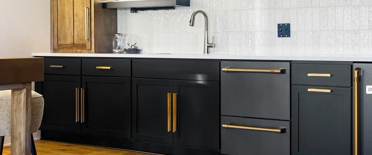 Stylish home bar with black cabinets, gold hardware, floating shelves with liquor bottles, and a modern tiled backsplash.