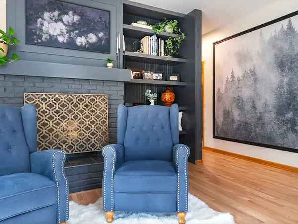 Elegant living room with blue armchairs, dark built-in bookshelves, and a large monochrome art piece.